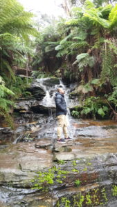 Man standing in front of a waterfall with his hands wide out and back towards the camera